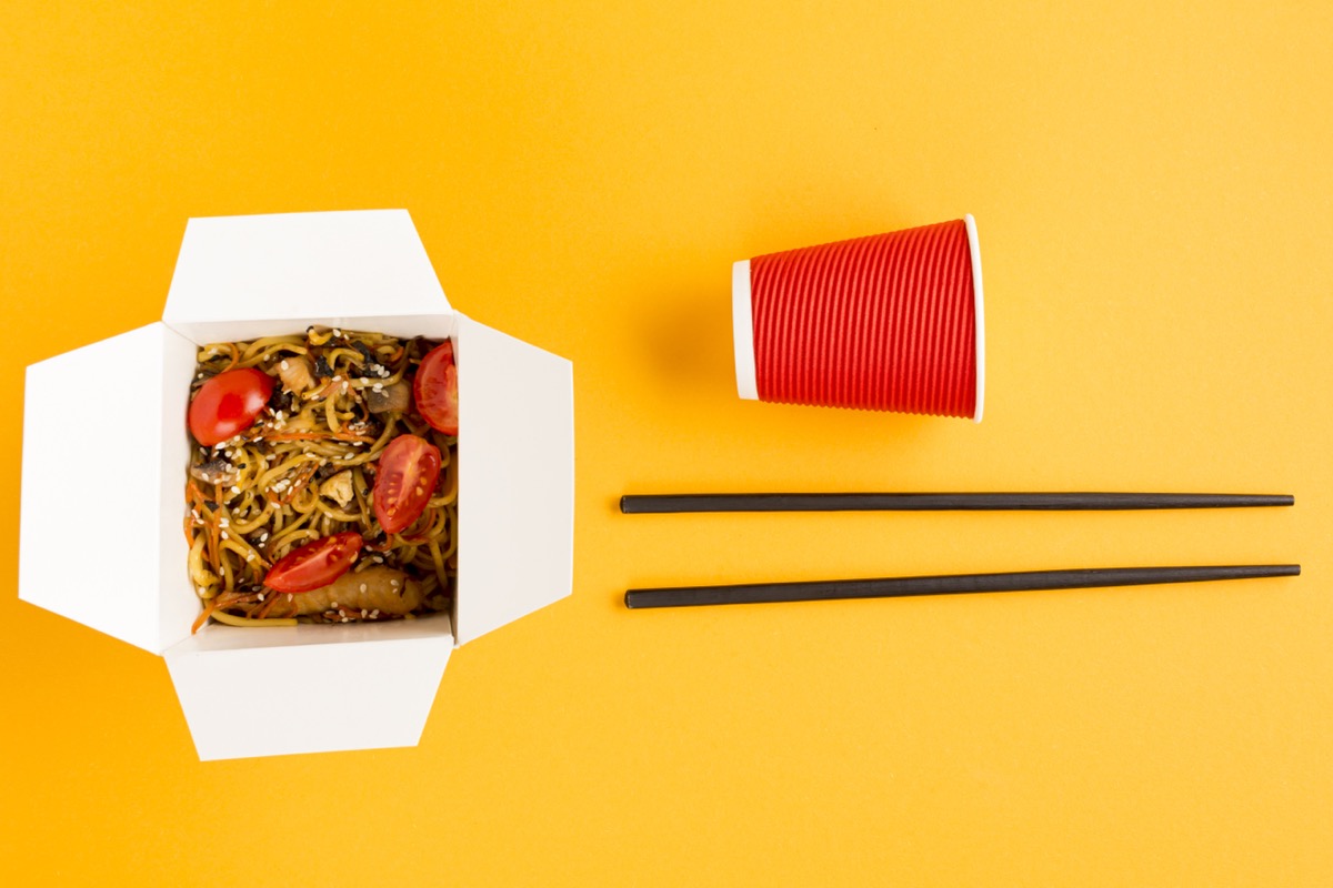 Noodles in a Chinese takeout box with chopsticks and a red cup