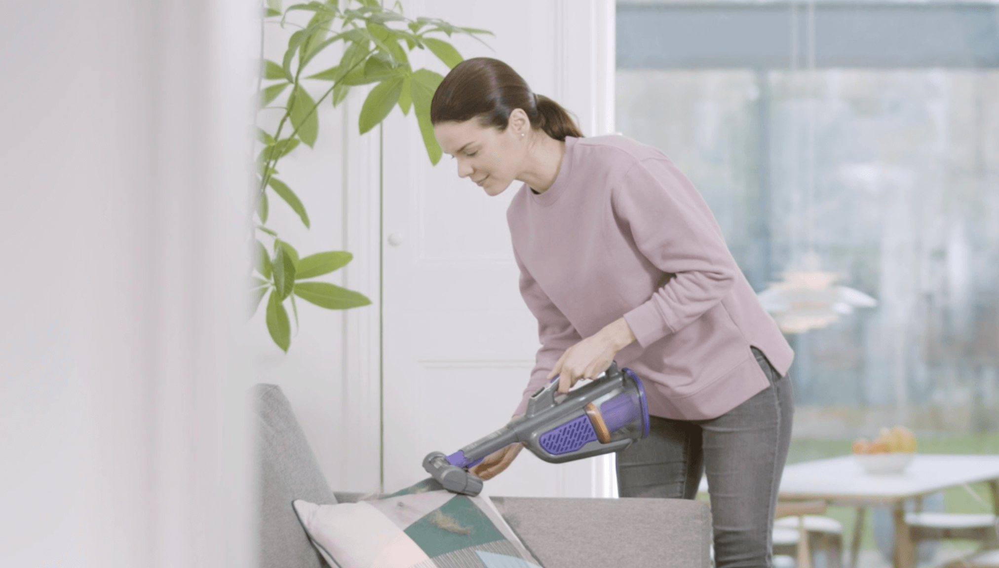 Woman vacuuming couch with handheld vacuum