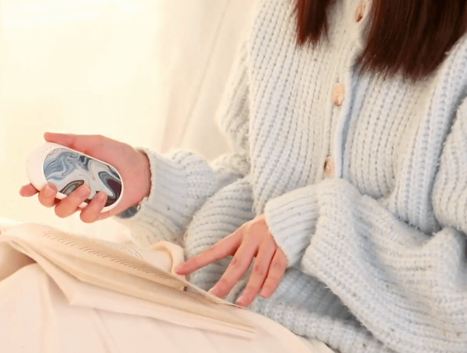 Woman holding rechargeable hand warmer while reading