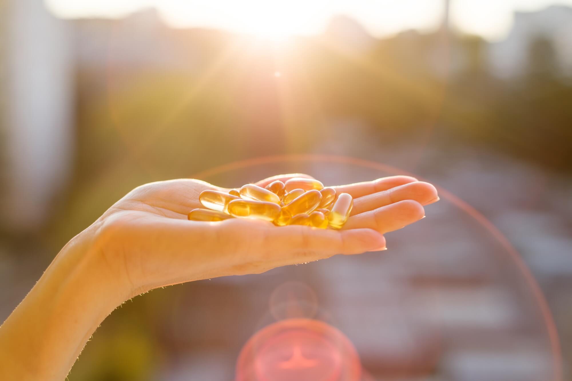 Hand of a woman holding vitamin D capsules, urban sunset background. 