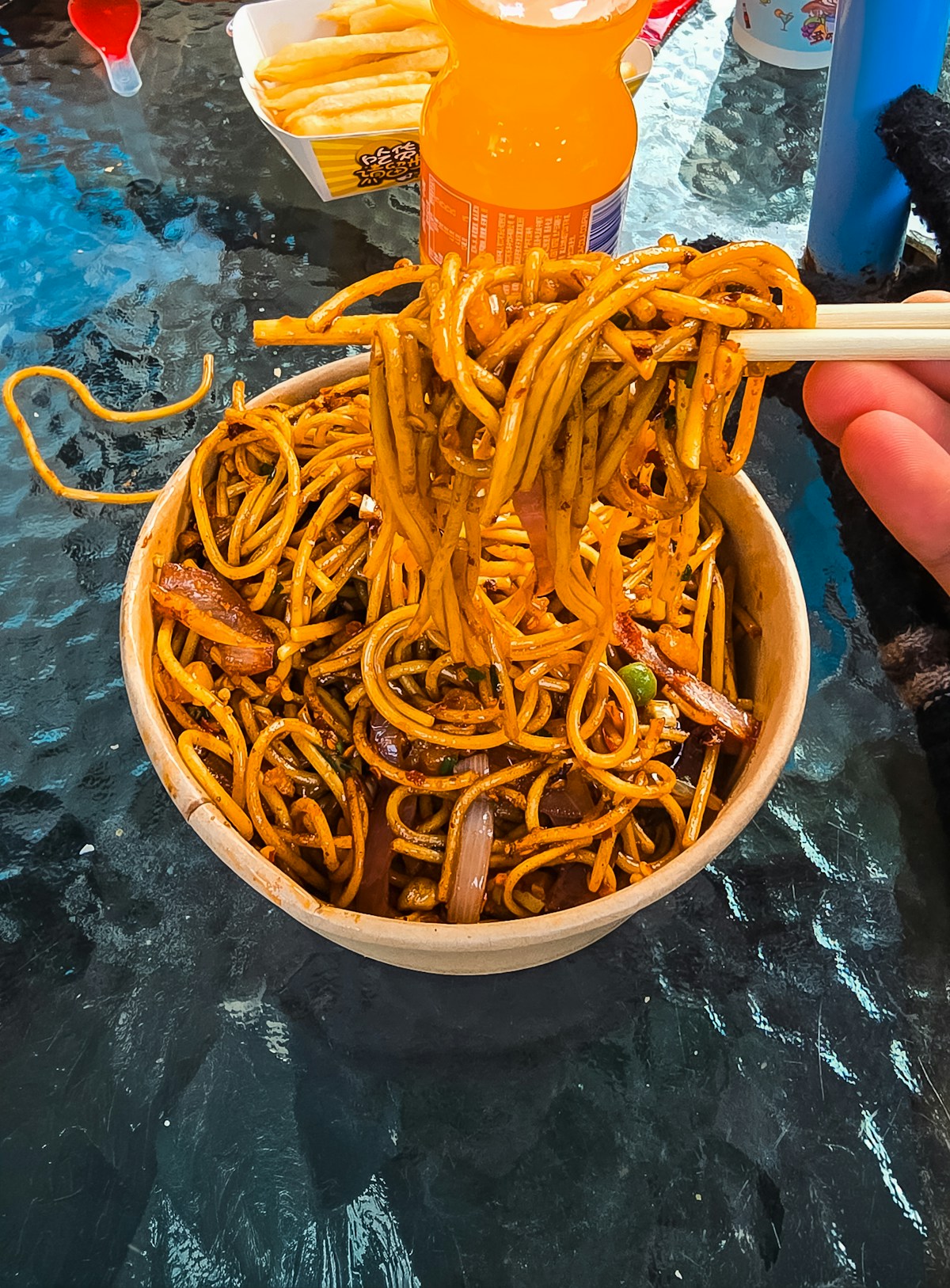 Stir-fried noodles lifted with chopsticks from a takeout bowl