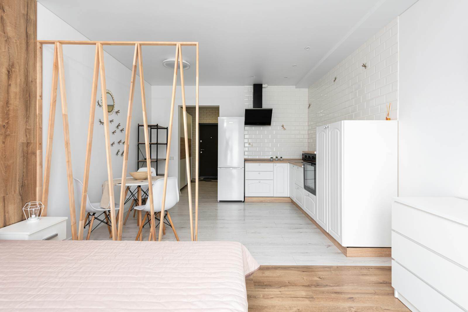 Bright minimalist studio apartment with a wooden lattice divider separating the bed from a small dining area and an open kitchen along the back wall