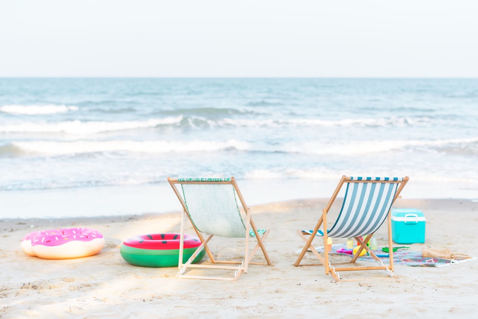 Two beach chairs and colorful inflatable floats set up on the sand facing the water on a bright summer day