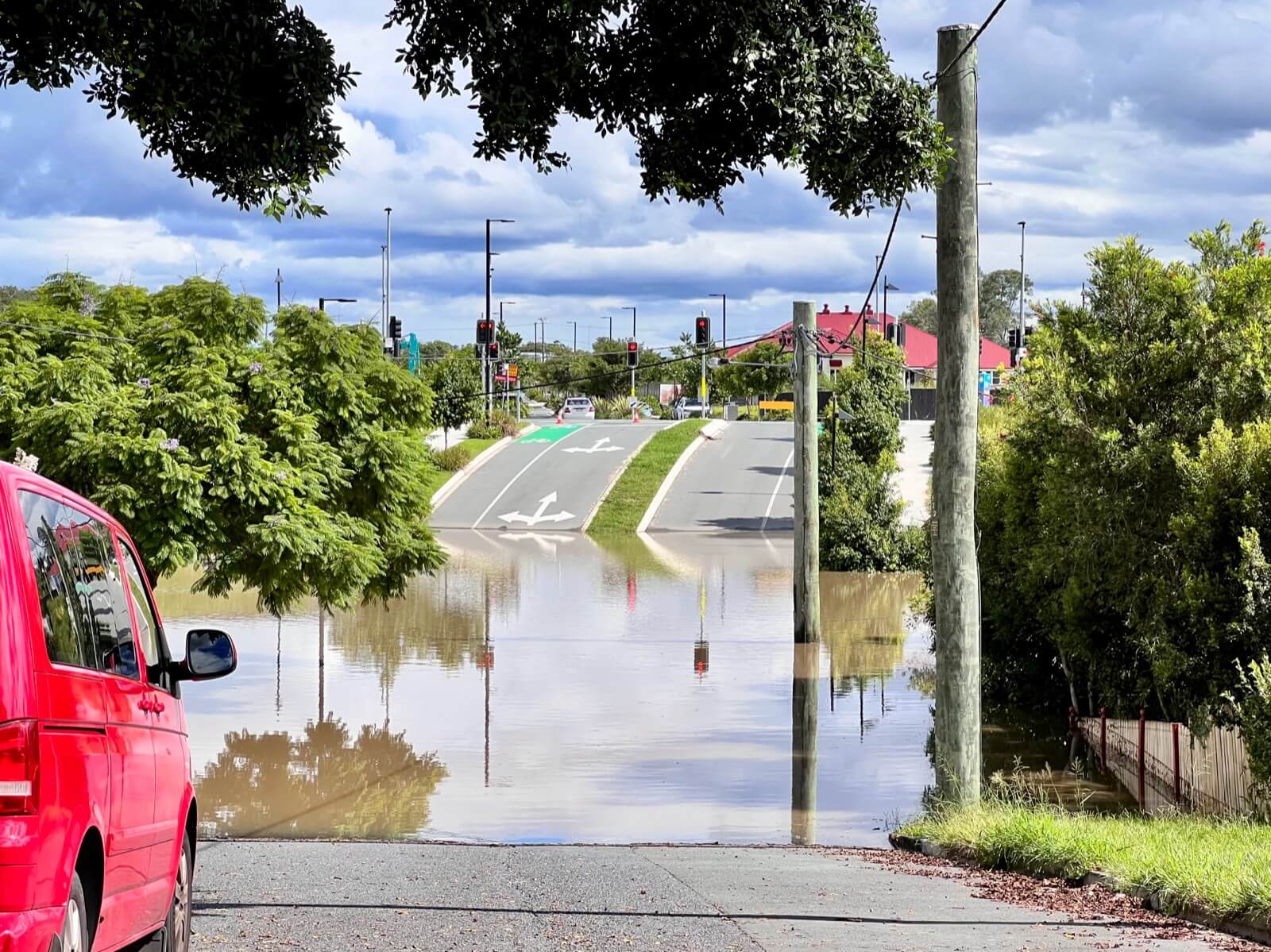 A suburban street in Yeronga, Brisbane submerged under brown floodwater during the 2022 Queensland floods, with traffic lights and a parked van above the waterline