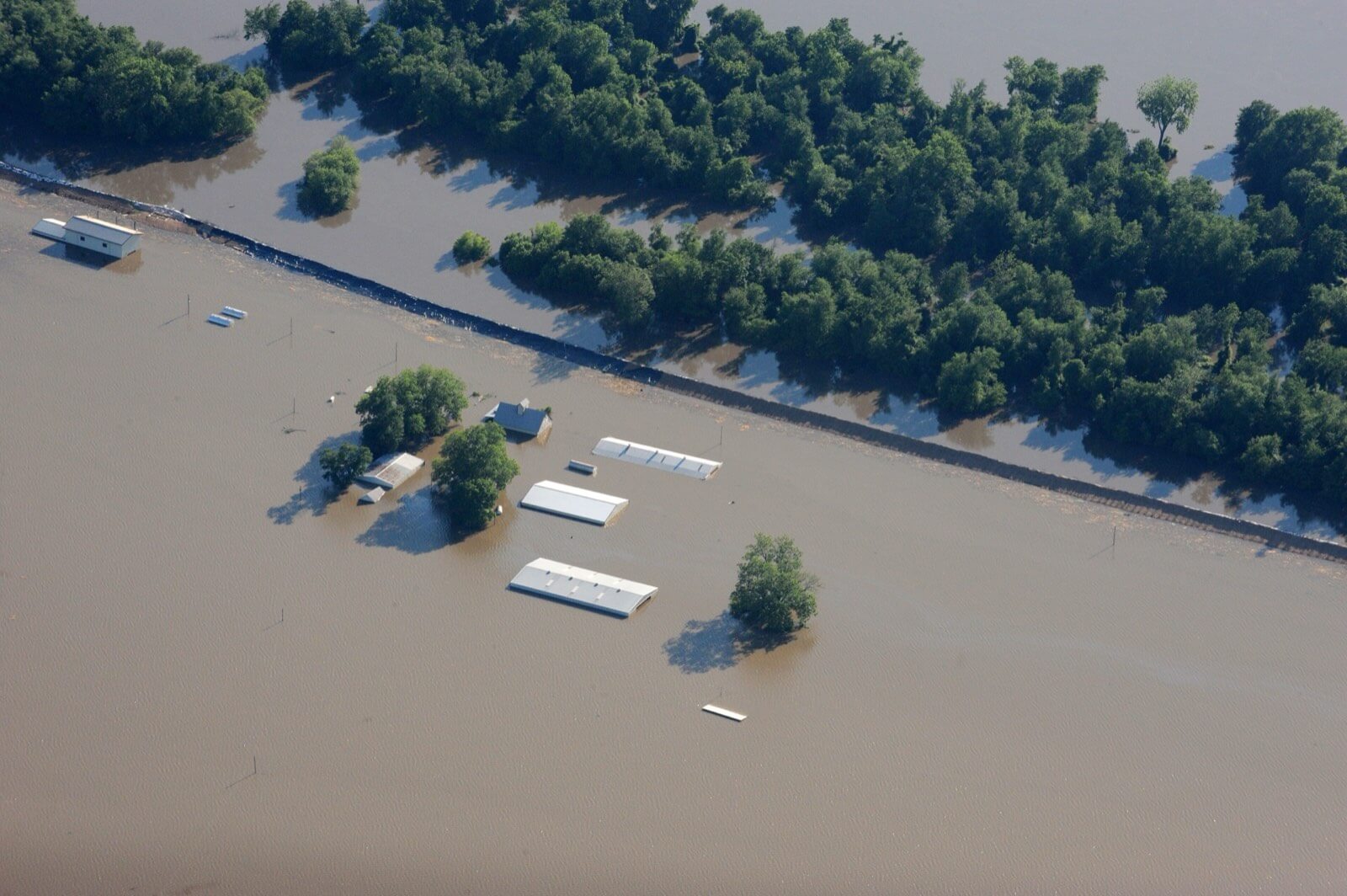 Aerial view of farm buildings submerged almost to their rooflines in brown floodwater across inundated farmland in Missouri
