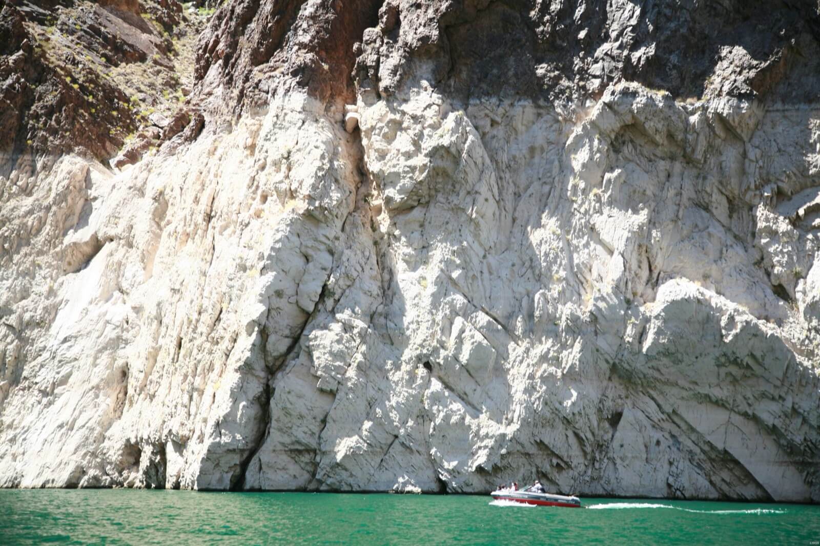 A small motorboat dwarfed by a towering pale mineral bathtub ring on the canyon wall at Lake Mead, marking how far the reservoir has dropped