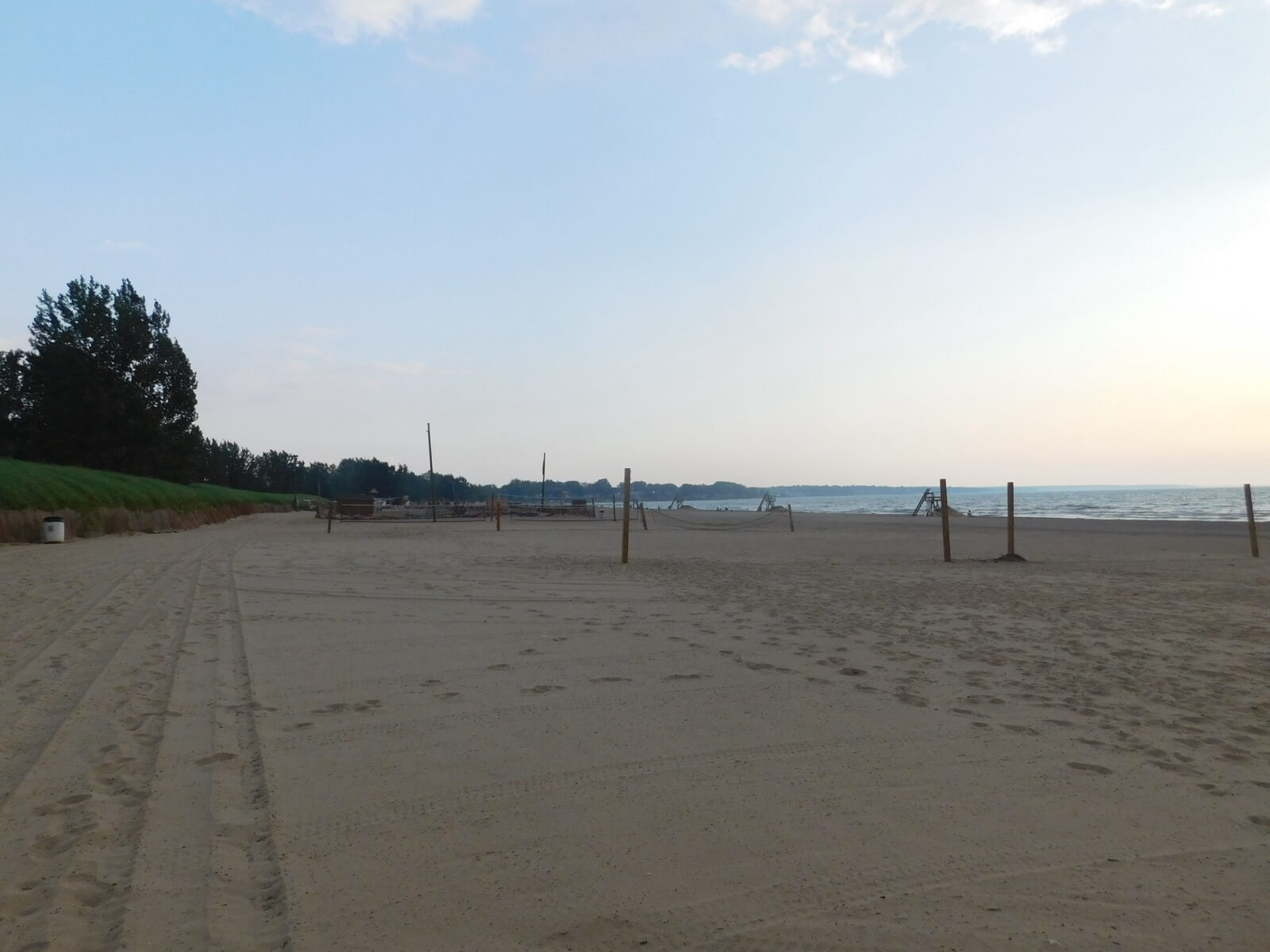 The wide sandy shore of Woodlawn Beach State Park meeting the calm blue water of Lake Erie under a partly cloudy sky