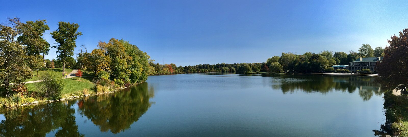 A wide panoramic view down the length of Hoyt Lake in Delaware Park on a clear October day, with autumn trees along both banks reflected in still water